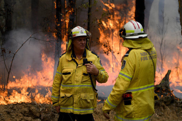 NSW Rural Fire Service crews talk as flames burn in the background.