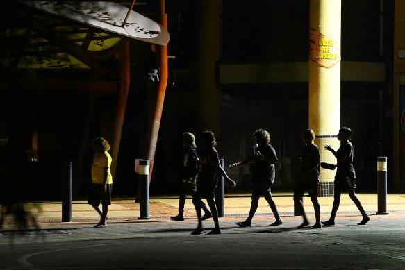 A group of people of mixed ages walking in the central business area of Alice Springs at night. 