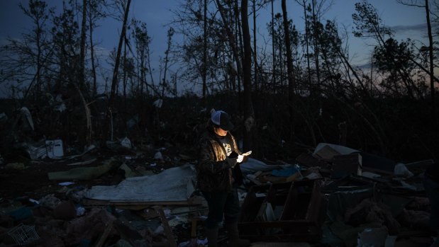 Matthew Schell looks for personal mementos by flashlight at dusk in the rubble of the house destroyed by a tornado.