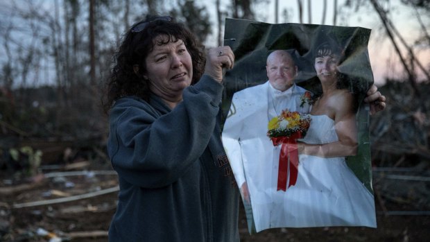 Carol Dean holds up her wedding photo to show family members after finding it in the rubble of the home she shared with husband, David Wayne Dean, who died when a tornado destroyed the house in Beauregard, Alabama.