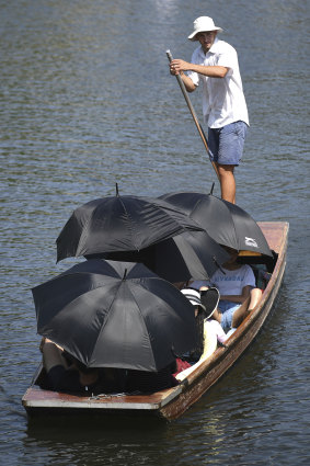 People shelter from the sun under umbrellas as they take a punt ride on the river Cam at Cambridge, England.