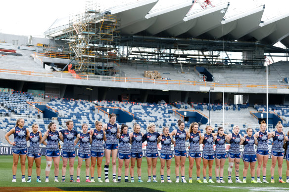 Under construction: Geelong’s AFLW team with the new stand being built at GMHBA Stadium in the background.