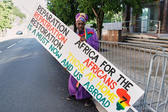 Jevon Thompson, of the Ethiopian African Black International Congress, carries a protest sign calling for reparations and a public apology while Charles was in Nassau on Wednesday.