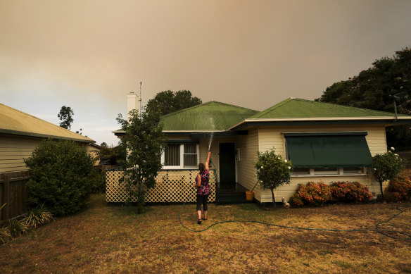 Bruthen resident Janine Pratt hoses down her home as burnt leaves fall on the property.