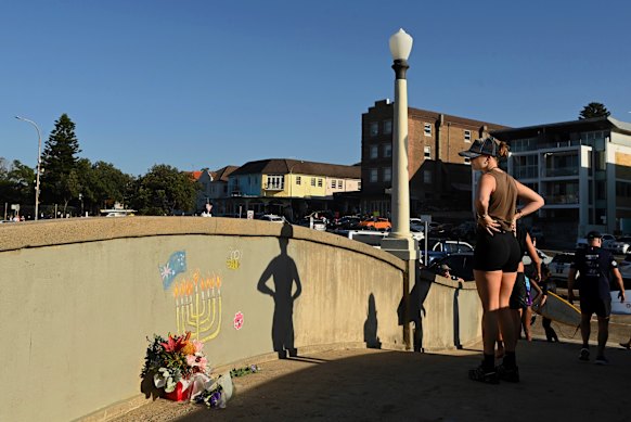 People walk past flowers and a chalk drawing of a menorah on the pedestrian bridge at Bondi Beach, where gunmen fired upon a Chanukah by the Sea crowd. 