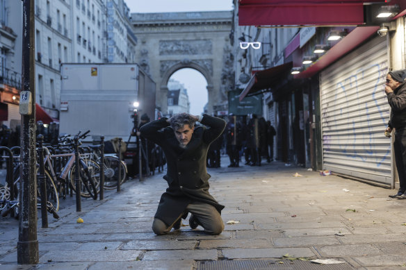 A member of Kurdish community kneels on the ground as he is detained during clashes stands with police.