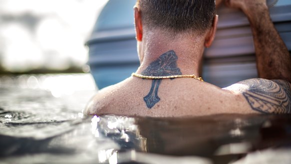 A tattoo of a cross decorates the neck of Walter Denton as he rests on the side of a boat while swimming in the ocean with his brother in Agat, Guam.