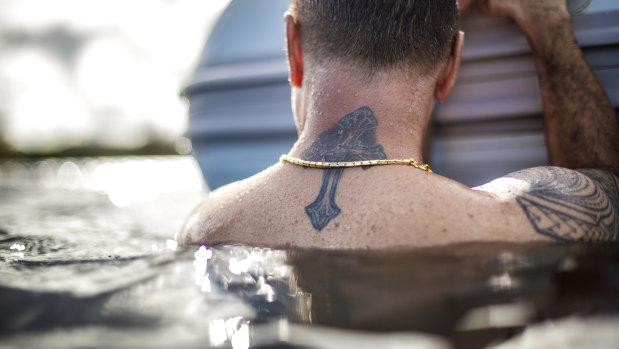 A tattoo of a cross decorates the neck of Walter Denton as he rests on the side of a boat while swimming in the ocean with his brother in Agat, Guam.