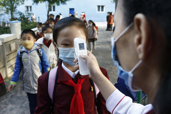 teacher takes the body temperature of a schoolgirl to help curb the spread of the coronavirus before entering Kim Song Ju Primary School in Central District in Pyongyang.