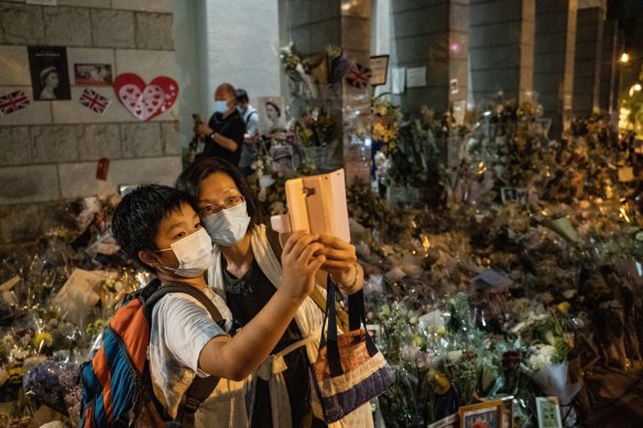 People pose for a selfie in front of the flower tributes outside the British Consulate in Hong Kong.