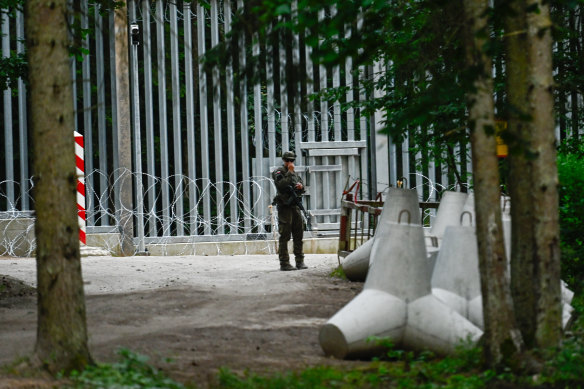 A soldier stands at the Polish border with Belarus, fortified with a metal wall and anti-tank obstacles.