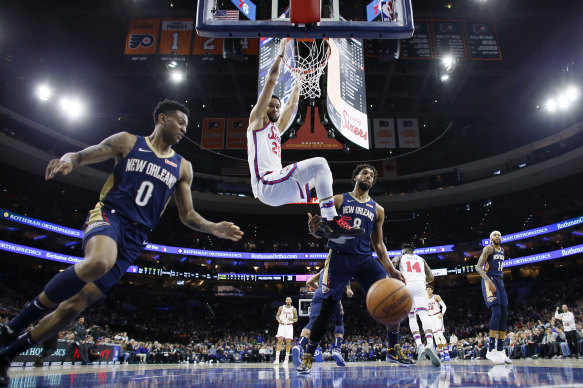 Ben Simmons hangs from the rim after a dunk past New Orleans Pelicans' Nickeil Alexander-Walker and Jahlil Okafor. 