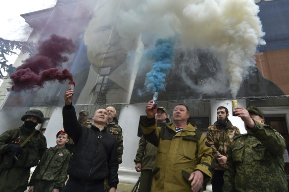People hold flares in colours of the Russian national flag during an action to mark the ninth anniversary of the Crimea annexation from Ukraine with an image of Russian President Vladimir Putin.