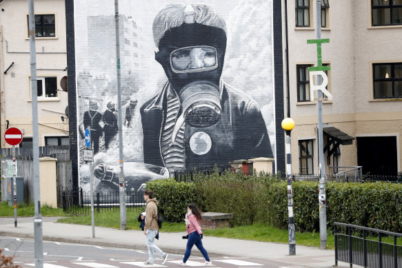 People walk past a mural depicting the Battle of the Bogside on a wall in Londonderry, Northern Ireland.