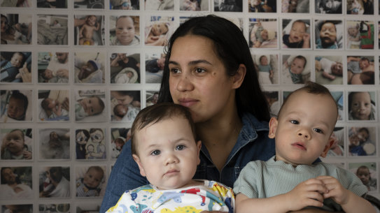 Elizabeth Tierney with her sons, Beau and Zane, in front of a photo collection of her first son, Cooper, who died at 6 months old from mitochondrial disease.