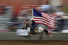 A horse rider carrying the American flag at a rodeo in the USA.