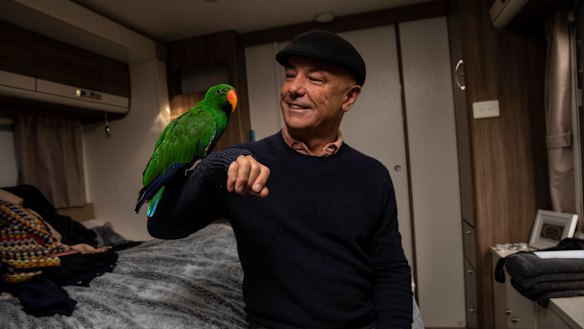 Geoff Belmore and parrot George sit in his temporary caravan.