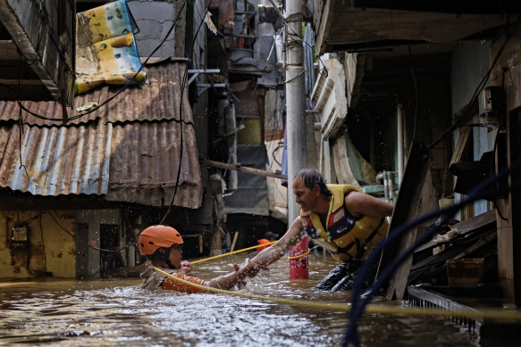 A rescue worker helps his colleague as they navigate a flooded Jakarta neighbourhood on January 2.