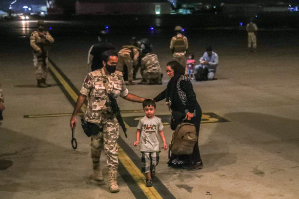 A member of the Qatar Air force walking next to a boy evacuated from Afghanistan, at Al-Udeid airbase.