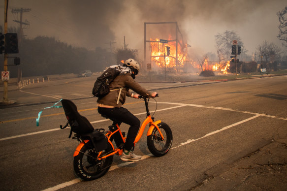 A man rides a bike while flames burn a building on Sunset Boulevard.