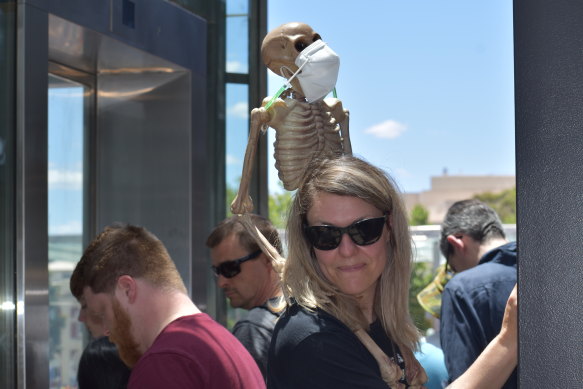 A woman holds a skeleton with needles, imitating the COVID-19 vaccine, and a face mask 