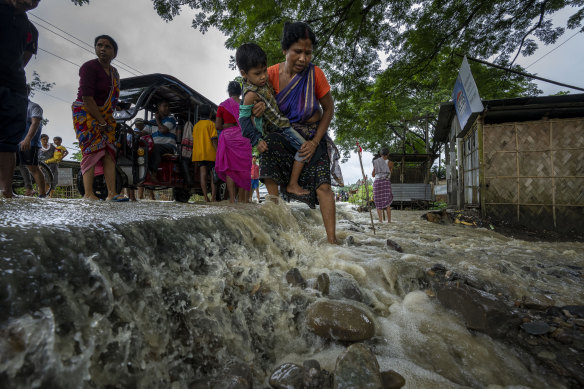 Families ford roads broken by floodwaters in Korora, wets of Gauhati, India.