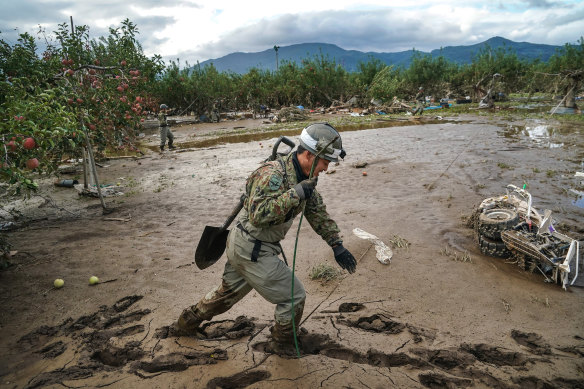Rescue personnel walk over a sea of mud near an orchard in Nagano, Japan.