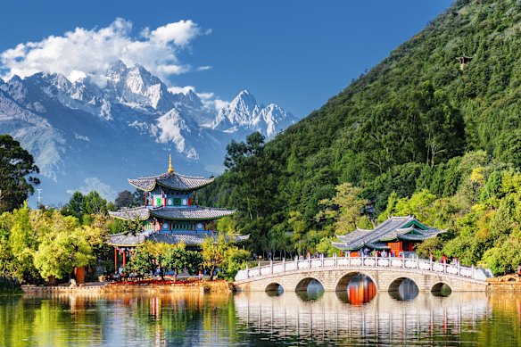 The Jade Dragon Snow Mountain provides an ethereal backdrop to the Black Dragon Pool and the Suocui Bridge, in Lijiang, China.