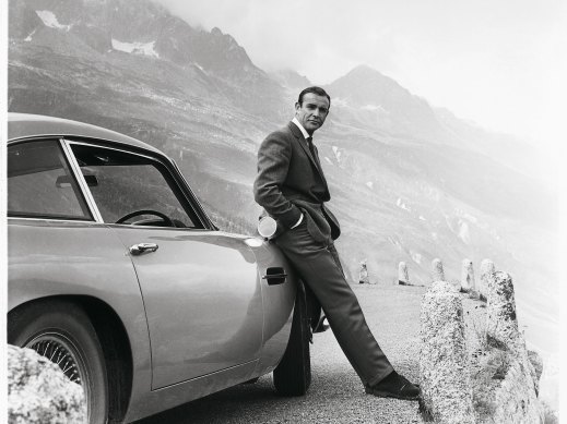 Sean Connery relaxes on the bumper of his Aston Martin DB5 during the filming for Goldfinger in the Swiss Alps.