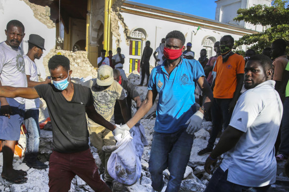 People carry away a body recovered from the rubble of an earthquake destroyed home in Les Cayes, Haiti.