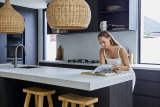 “Because of the open-plan living, and because there’s only two of us, we have all our meals at the kitchen bench,” says Kate. “It is one of my favourite spots.”  The kitchen bench is Caesarstone in “Cloudburst Concrete”, the lampshades are from Ur Place and the wooden stools are by Uniqwa Collections.