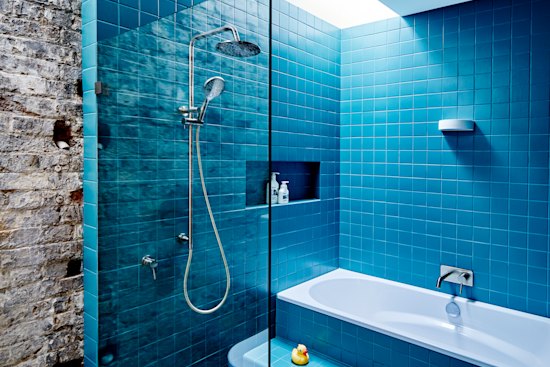 A doorway from the kitchen leads to a family bathroom. Part of the original stable wall is exposed, offering a textural contrast to the glossy tiles.
