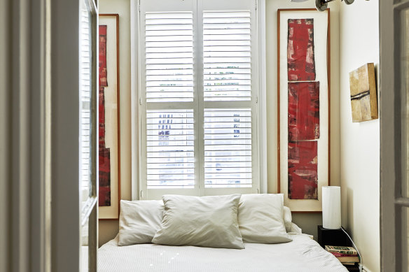 The bedroom features plantation shutters and is separated from the living room by a pair of French doors. The vertical artworks are by George Raftopoulos.