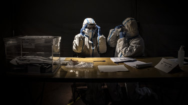 Election workers wearing protective equipment clean their fogged goggles while waiting for voters during the final hour of voting at a polling station during regional Catalan elections in Barcelona, Spain. 