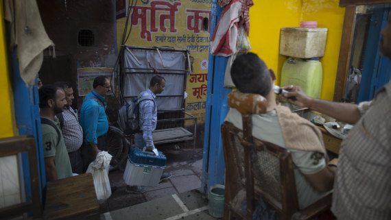 Election officers carrying electronic voting machines walk past a barber shop at the close of polling in Varanasi, India on Sunday.