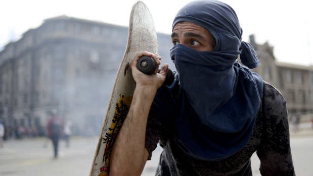 An anti-government protester peers out from behind his skateboard during clashes with police in Valparaiso.