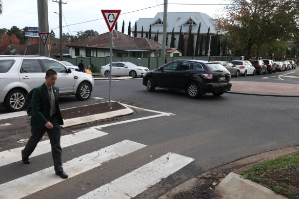 A student crosses the road as cars queue for the pick-up zone at James Ruse and Carlingford West Public School.