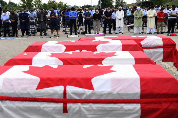 Mourners pray as caskets draped in Canadian flags are lined up at a funeral for the four Muslim family members killed by a white nationalist in June 2021.