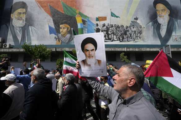 People walk past a mural showing Ayatollah Khomeini, right, Supreme Leader Ayatollah Ali Khamenei, left, while holding a poster of Ayatollah Khomeini and Iranian and Palestinian flags in an anti-Israeli march after Friday prayers in Tehran.