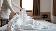 Woman making bed in bright bedroom. Maid Cleaning messy hotel bed cushion and duvet, changing bed sheets with clean. Selective focus. Copy space