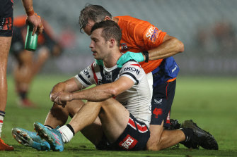 Roosters half Sam Walker receives attention from a trainer after being taken out by Tigers prop James Tamou.