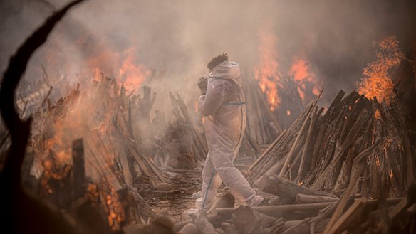 A worker wearing a protective suit is seen amid the burning funeral pyres of patients who died of COVID-19 at a crematorium in Delhi, India.