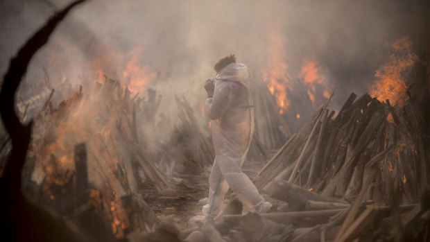 A worker wearing a protective suit is seen amid the burning funeral pyres of patients who died of COVID-19 at a crematorium in Delhi, India.