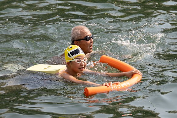 An old man and a young girl swim together.
