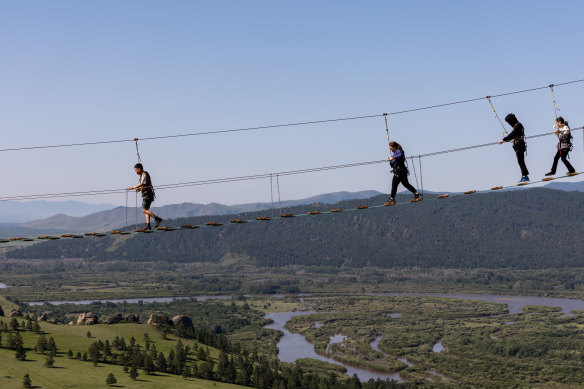 Mongolians walk over a bridge looking over Russian Siberia. 