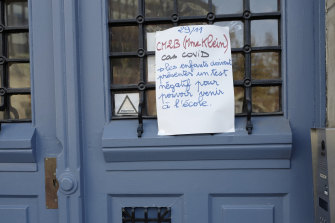 A note is fixed to the door of a school in Paris telling parents that a pupil has tested positive and that other students need negative tests to attend.