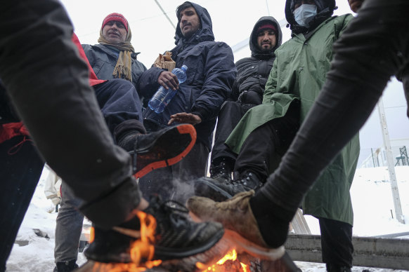 Men warm their feet at makeshift fires while they wait for food parcels. 
