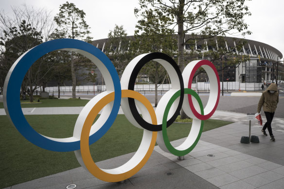 A man wearing a face mask walks past the Olympic rings in front of the main stadium for the Tokyo Olympics.