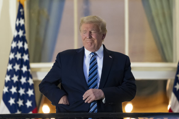 US President Donald Trump puts his mask in his pocket as he stands on the Blue Room Balcony at the WHite House after leaving hospital.