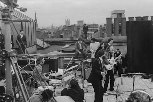I Beatles si esibiscono dal vivo sul tetto dell'edificio Savile Row a Londra nel 1969. Il batterista Ringo Starr siede dietro la sua batteria, i cantautori Paul McCartney e John Lennon si esibiscono ai loro microfoni, mentre il chitarrista George Harrison sta dietro di loro. La moglie di Lennon, Yoko Ono, siede a destra.